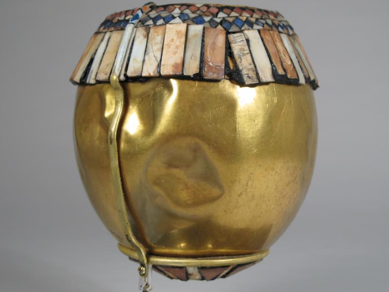 Gold ostrich egg with shell inlay around the rip in striped and diamond patterns.