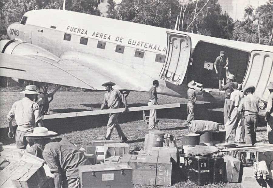 A group of people unloading cargo from a plane into a clearing.