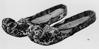 Pair of figured brocade slippers found together with a pair of brocade socks in 1966 in a tomb dated A.D. 778 in a cemetery in Astana, near the town of Turfan in th northeastern part of the Tarim basin (Sinkiang Ulighur, Autonomous Region). This is a place along the ancient silk route from China to the West. Different materials were used for the outside and the lining of the slippers. The latter is actually not made of one material but stitched together of a number of differently patterened silks. The colors used include red, white, black-brown, green, yellow, bright blue, and pink and they have kept brightness over more than a thousand years. Pottery figurines of the Sui and T'ang periods show ladies wearing the same type of shoes with upturned, so-called lotus of cloud, toes. T'ang period, 8th century A. D. Wên-wu 1972 No. 3. 