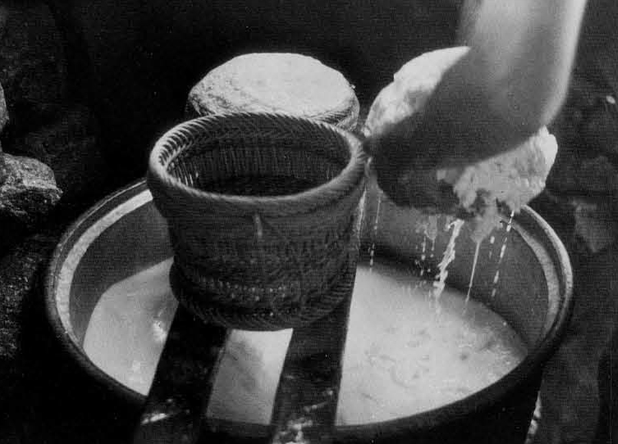 Figure 10. Gathering curdled cheese from the cauldron. Baskets rest on the wooden frame. 