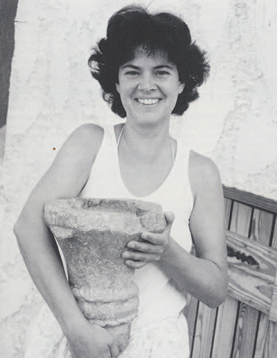 Teresa Howard, chief artist for the Pseira excavations, holds a large serpentine lamp. The lamp was found in the Plateia House, the largest building discovered on Pseira, where it had fallen from the second story. The reservoir in the upper surface of the lamp would be filled with fat or olive oil, and a burning wick added to create light. 