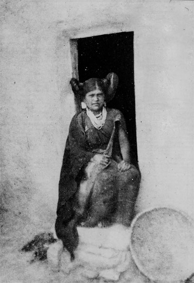 A girl seated in a doorway with an eleborate hair style.