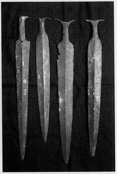 Four swords of roughly the same size and shape, raised ridge down the middle of each, flared handles.