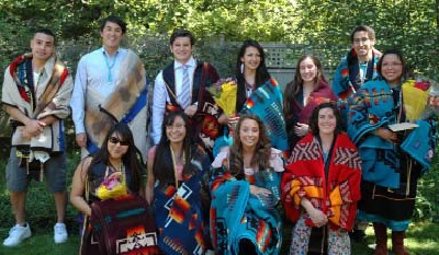 Group photo of new graduates, all wraped in colorfully patterned blankets.