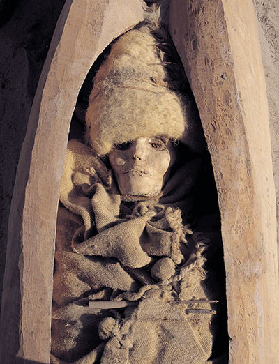 A mummified woman in a thick hat and cloak.