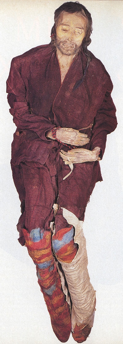 A well preserved mummy in a dark red robe and colorful stockings.
