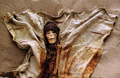 A mummy nestled in a blanket, wearing a hat.