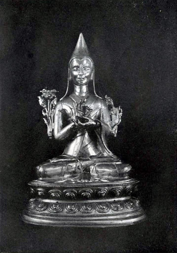 Gilded brass statuette depicting Tsongkhapa with hands in preaching mudra and lotus stalks at his shoulders, wearing a hat