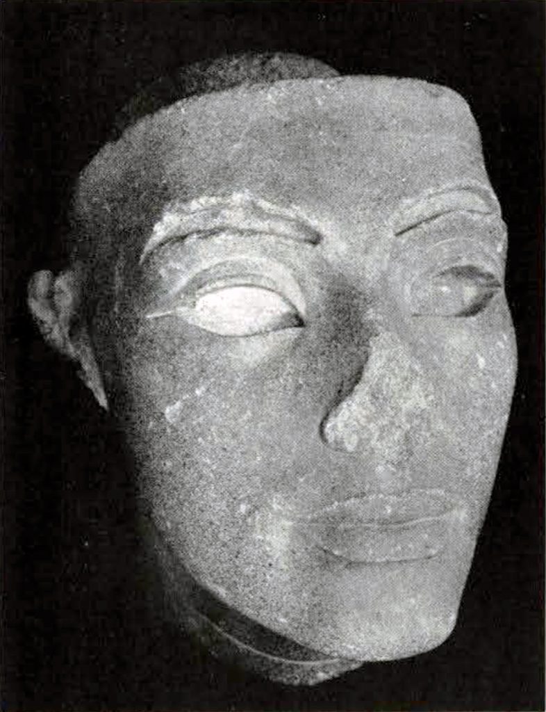 Large carved stone head with nose missing and winged eyes