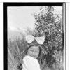 Sxe-la. Young female child sitting in undergrowth. Modern dress. large ribbon in hair. July 1918. Haines, Alaska.