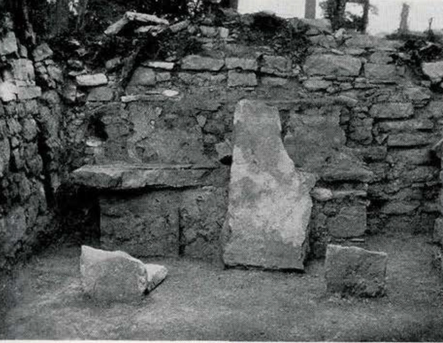 View of a stone throne with a slab leaning against it in a room with stone walls