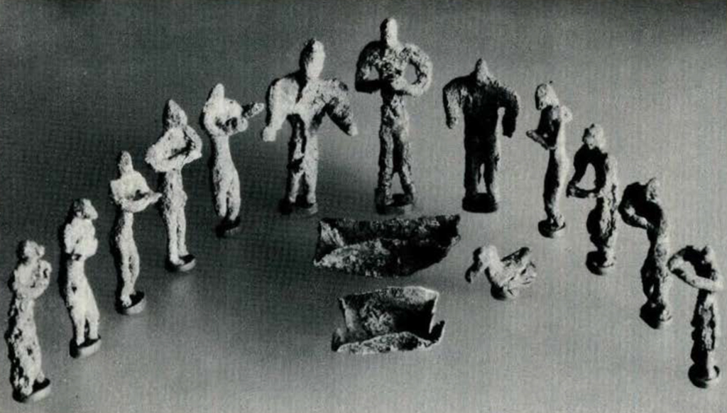 Twelve copper human figures arranged in a half circle with a copper duck