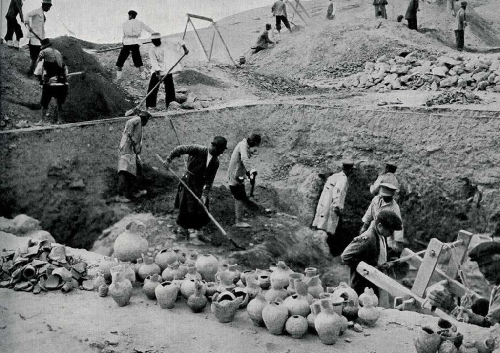 Men excavating a trash pit, a pile of vessels and vessel fragments in the foreground