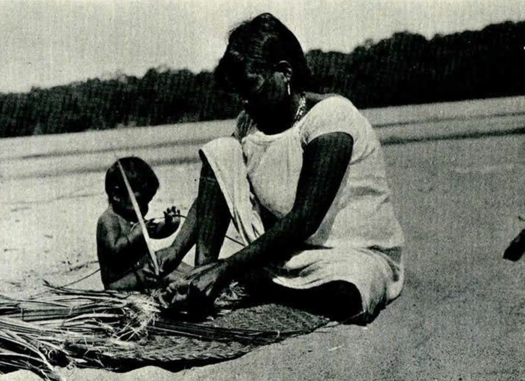 A woman weaving a basket with a child sitting nearby