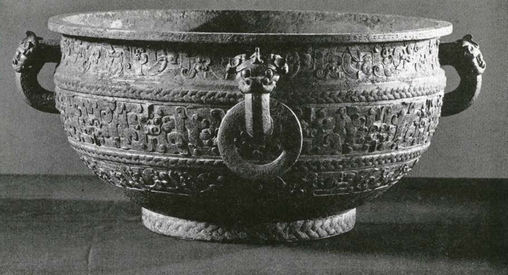 A shallow bronze bowl or cauldron with three registers of decoration and four handles