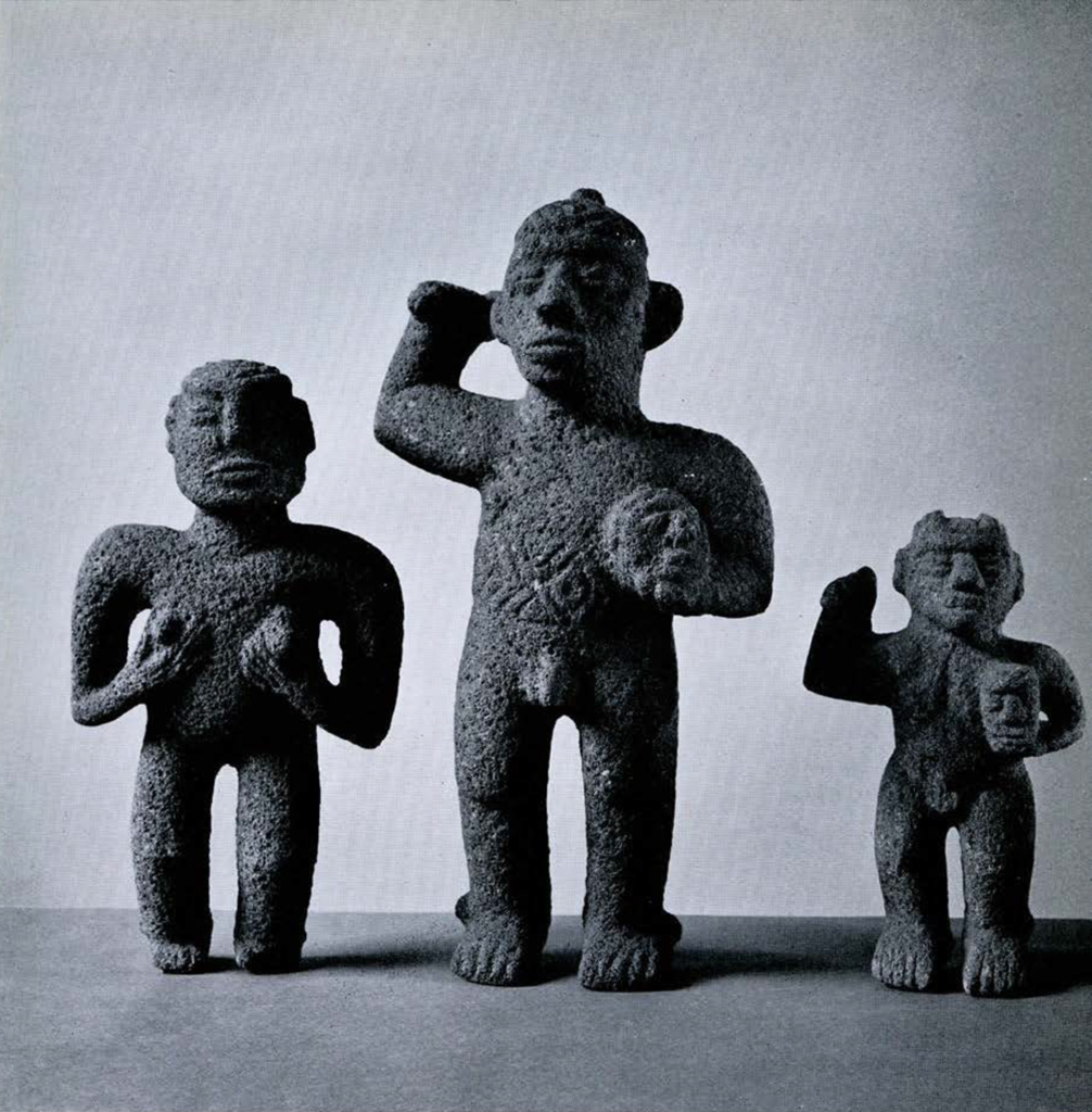 Three small figures carved out of lava stone, two with one arm raised and the other holding an object