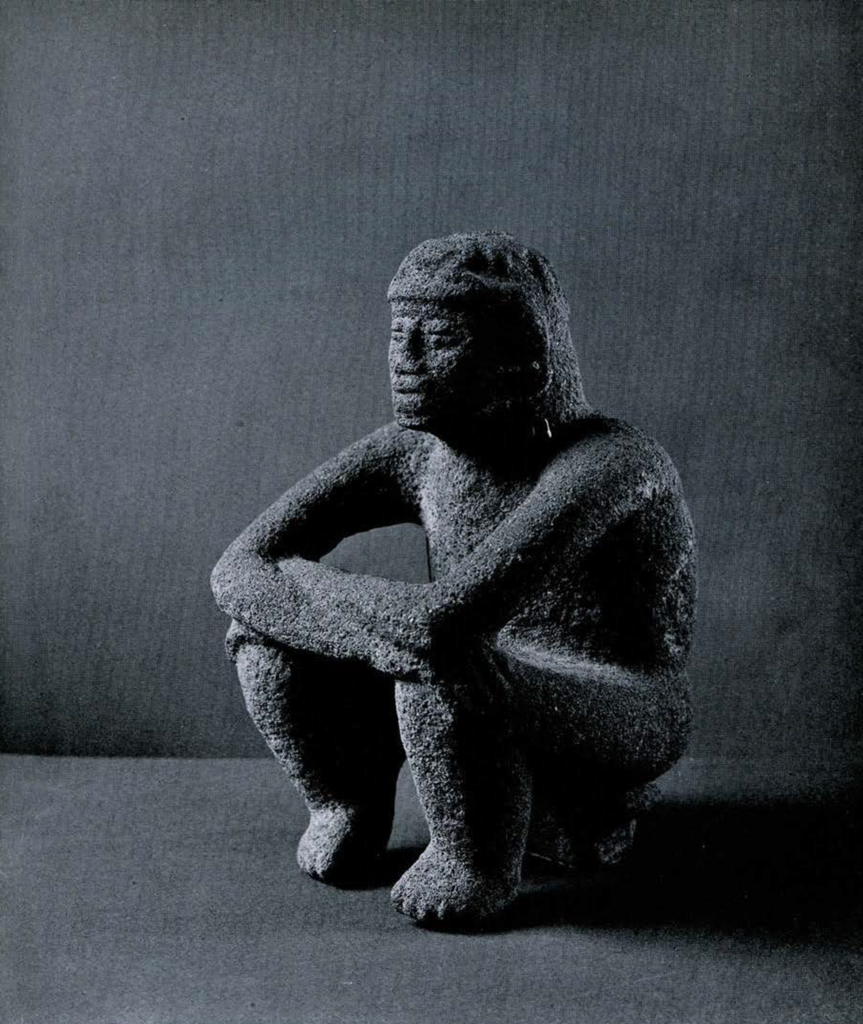 Carved lava stone figure of a squatting man with arms crossed atop his knees