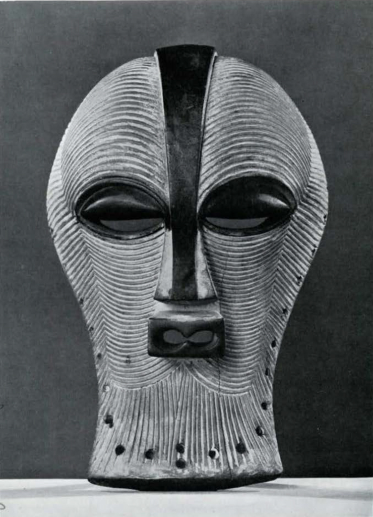 Wooden mask with eyes and nose, striations covering the rest, originating on the central vertical line