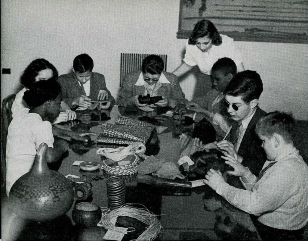 A group of blind children seated around a table, holding objects
