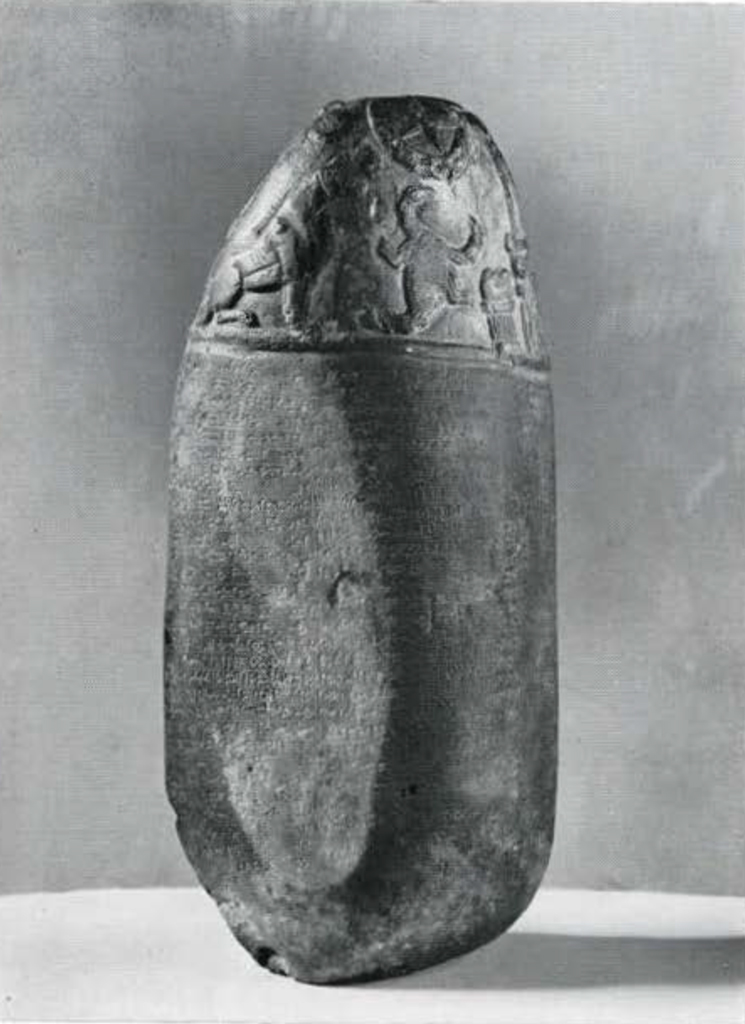 A boundary stone, lower two thirds inscribed, top third carved relief of a sitting dog and scorpion