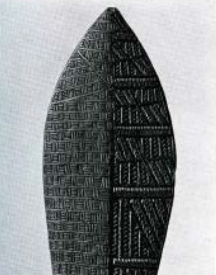 Close up of the head of a wood paddle, with two different geometric patterns carved into the two different vertical halves