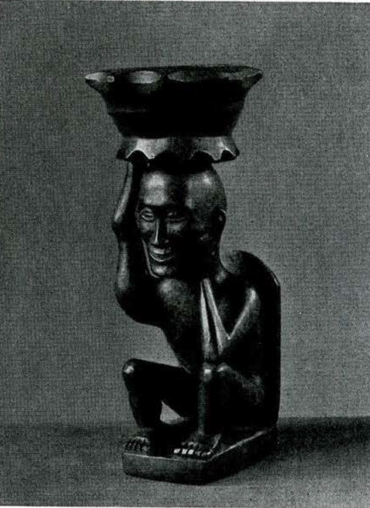 Figure of a man seated on a kind of legless chair supported on his head, with the help of his right hand, a small round vessel with scalloped rim and base; the elbow of his left arm rests on his knee and the hand is pressed against his left cheek.