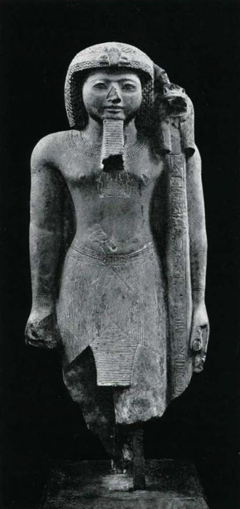 Statue of Rameses III wearing a false beard and short wig, a cobra diadem, a pleated kilt, he has a dagger and a lioness-headed staff.