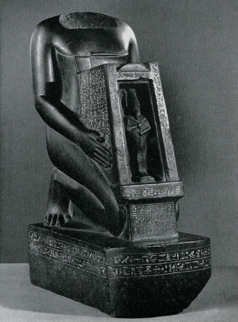 Statue of a priest kneeling and holding a small shrine that contains an image of the god Osiris, head of the statue missing.
