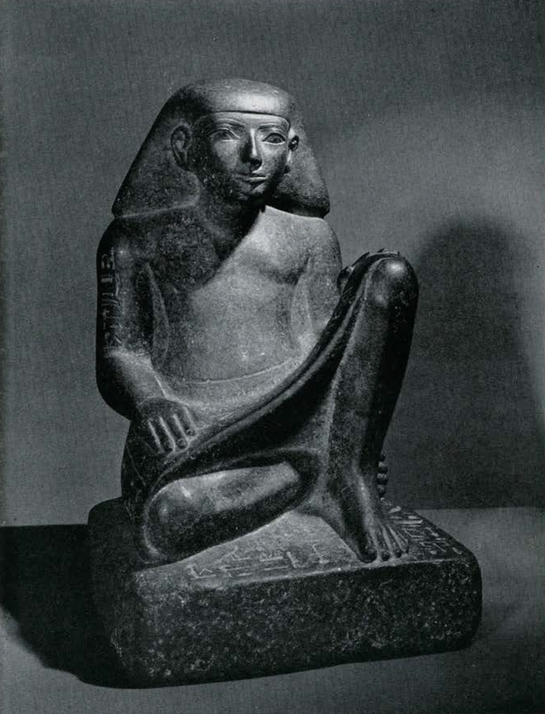 Seated statue of a scribe wearing a short kilt and a short wig, the lap, sides and base of the statue are inscribed with a text.