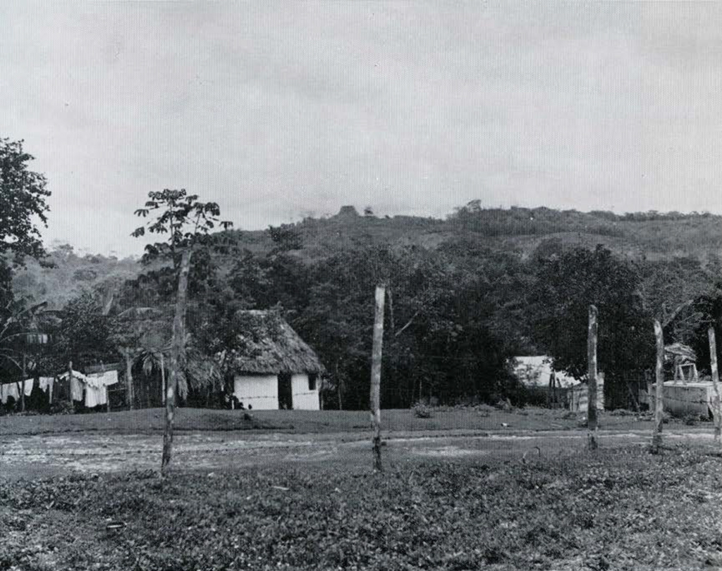 A small village with a mound and ruins in the background.