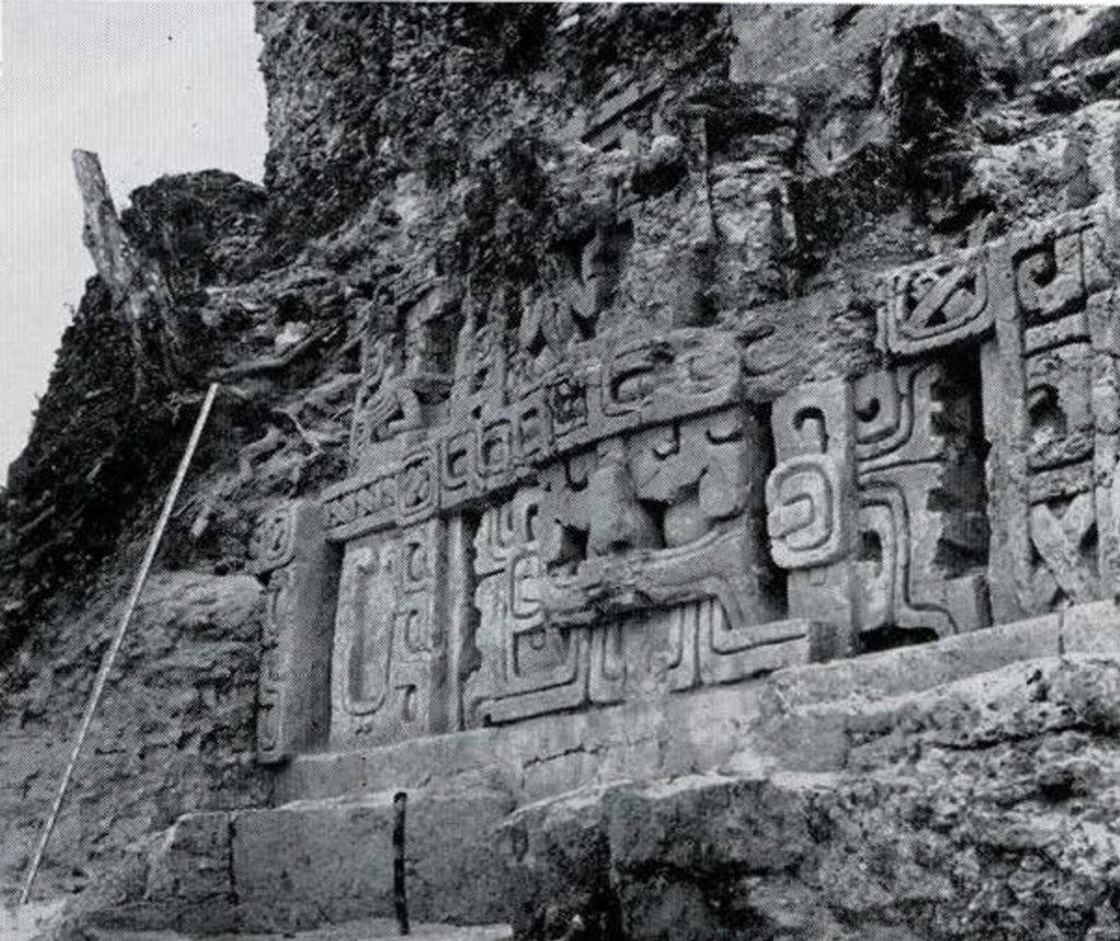 An excavated structure with large stone carvings, including the upper half of a stylized face.