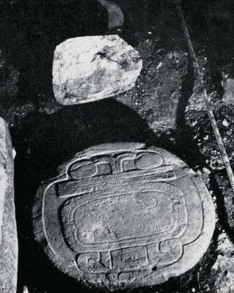 A rounded altar with a date glyph carved into the top, and a base of a stela.