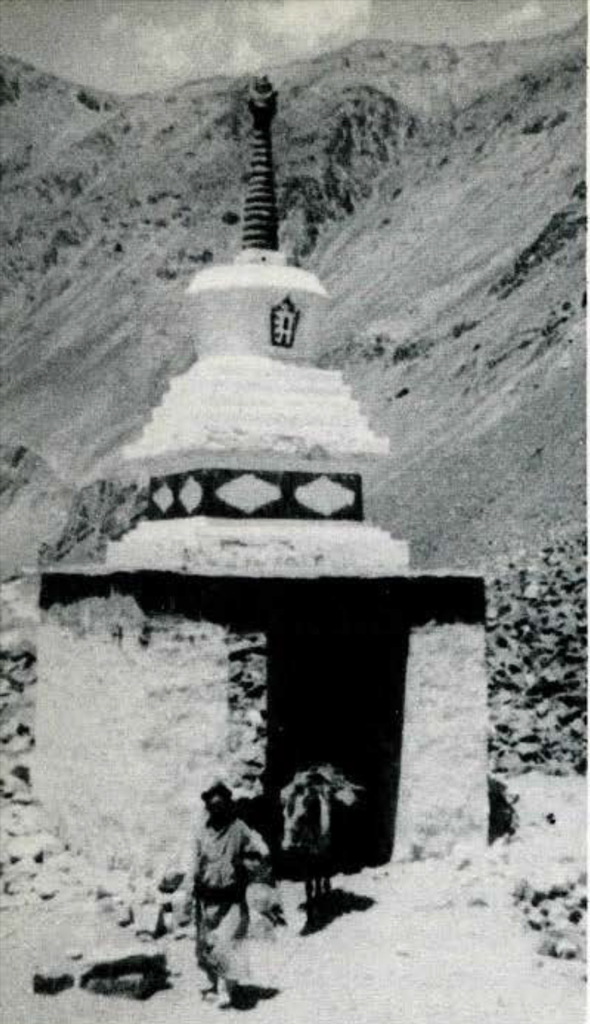 A stupa admist hills, people walking around it.