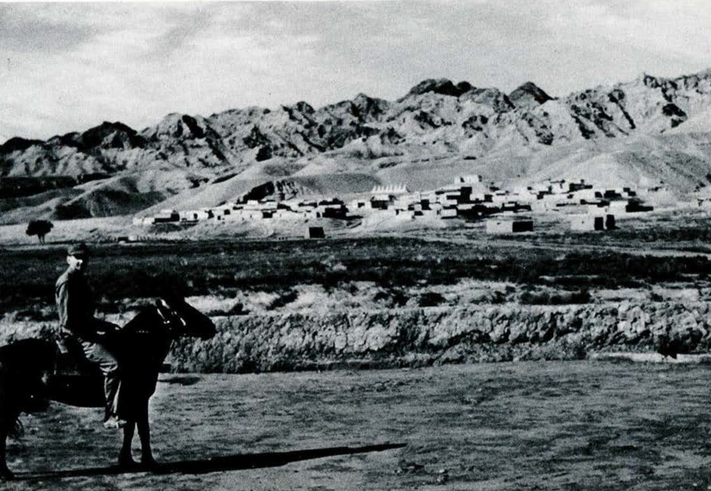 A man on horseback with Shandagu Monastery and mountains in the background.