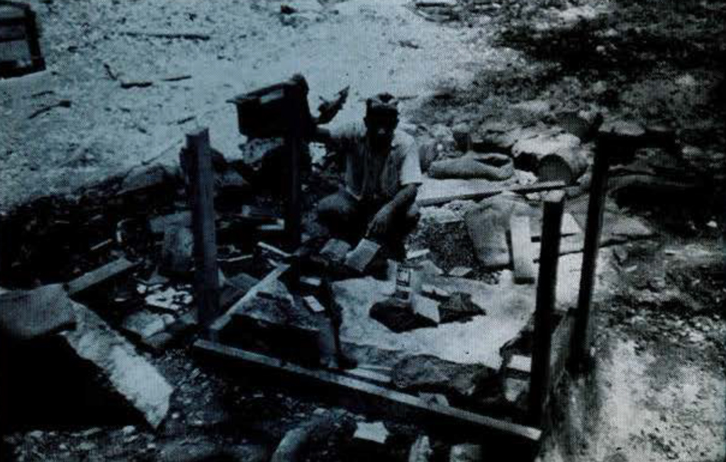 A person sitting on the ground, constructing a small wooden crate.