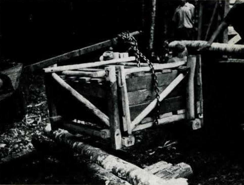 A woooden crate being hoisted by chains.