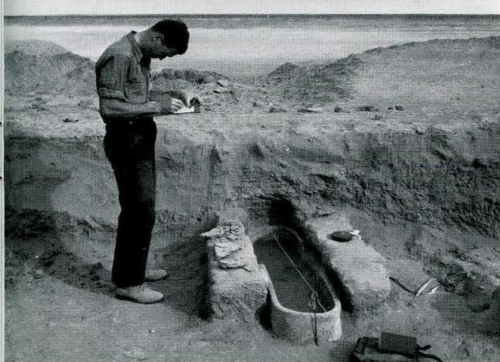 A man standing over an excavated burial, sketching in a book.