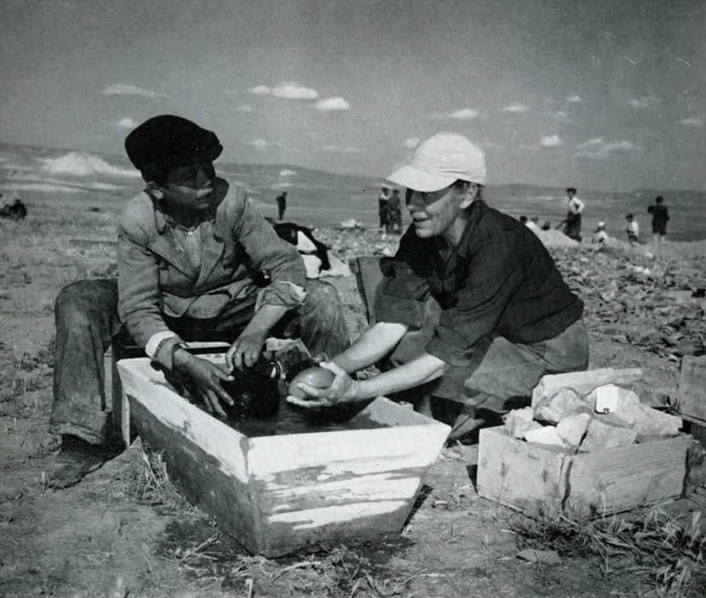 A woman and a young man cleaning artifacts in a wood tub.