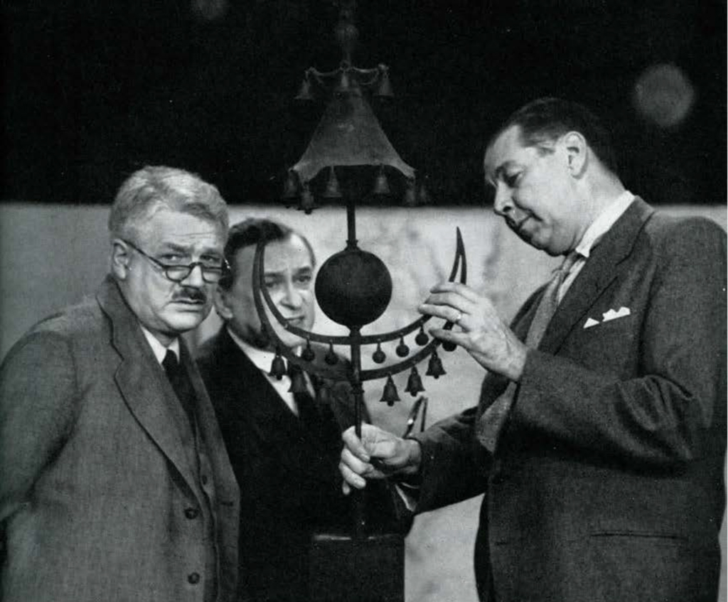 Three men axaming a object with many bells and a crescent moon shape.