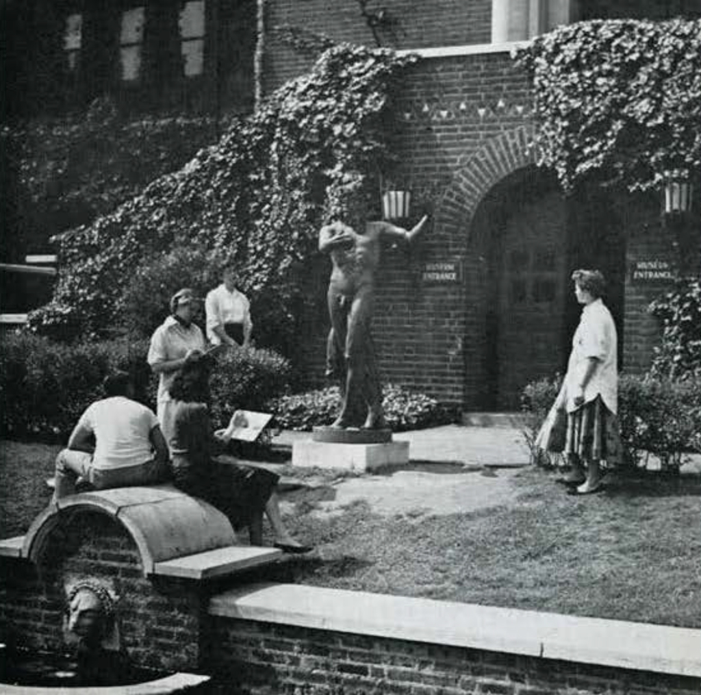 People in the courtyard garden, examining a statue and sitting by the fountain.
