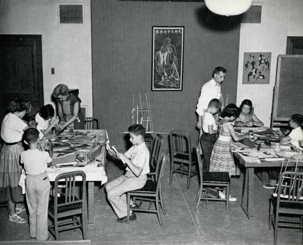 Groups of school children surrounding tables, doing crafts.