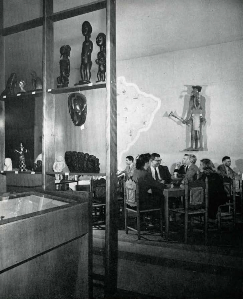 Groups of people seated as small tables in a coffee shop, artifacts on the walls behind them.