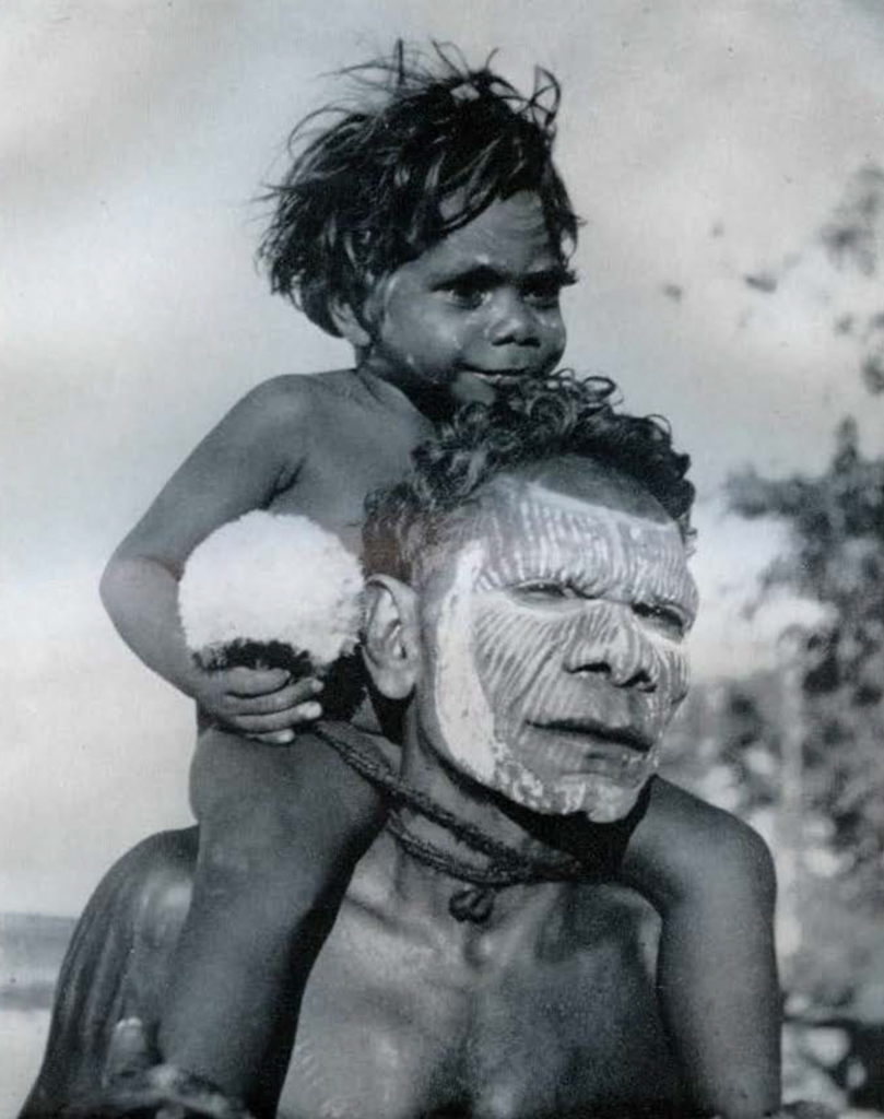 Tiwi man with painted face, and child sitting on his shoulders.