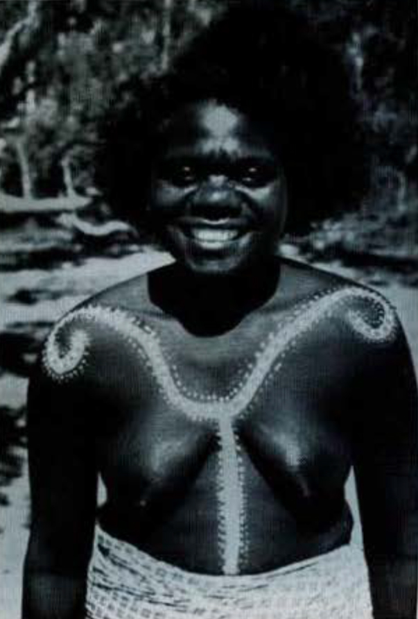 A woman smiling, with a painted curly line across her shoulders and verticlaly down her chest.