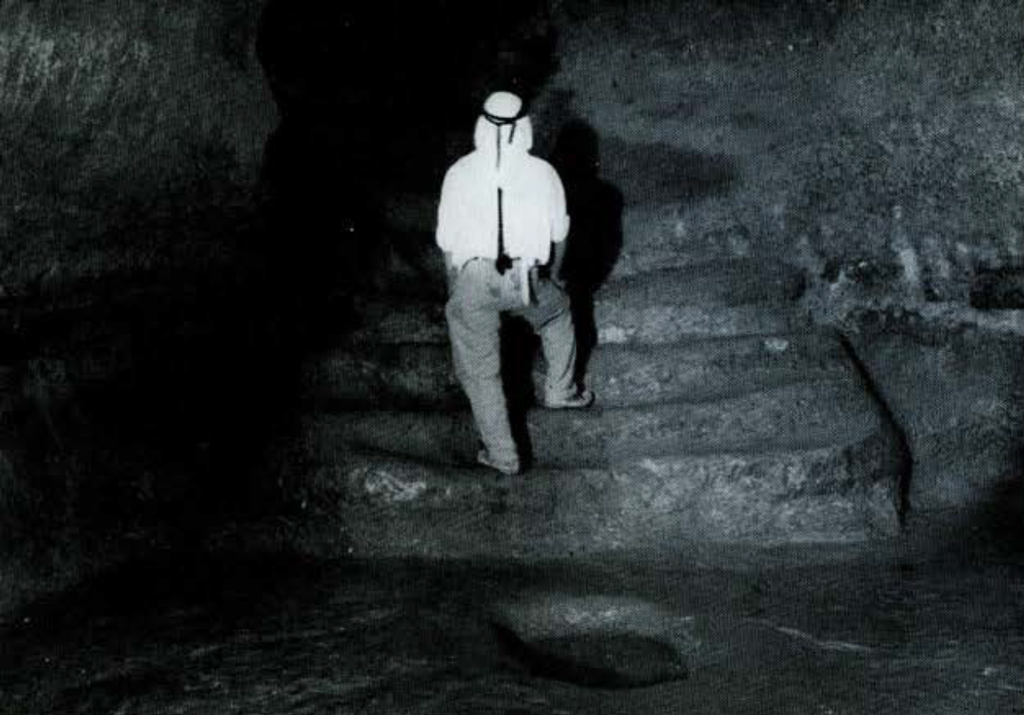 A man walking up rock cut stairs in a tunnel.