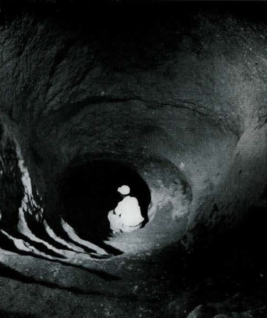 A man sitting on a rock cut groove of a tunnel leading down.