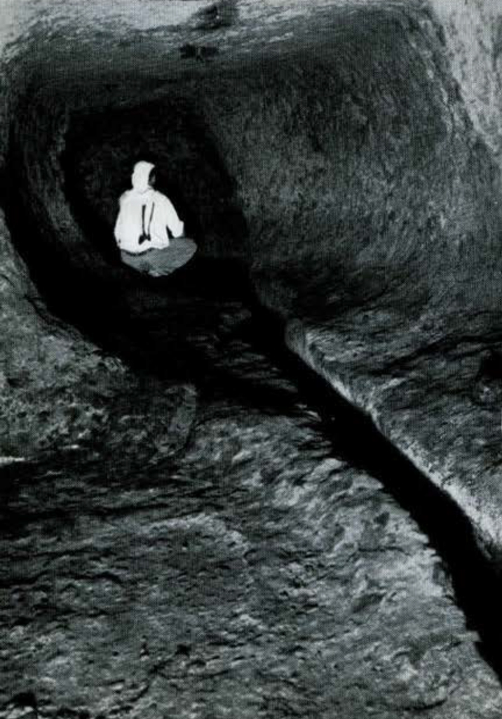 A man crouching in a low tunnel.