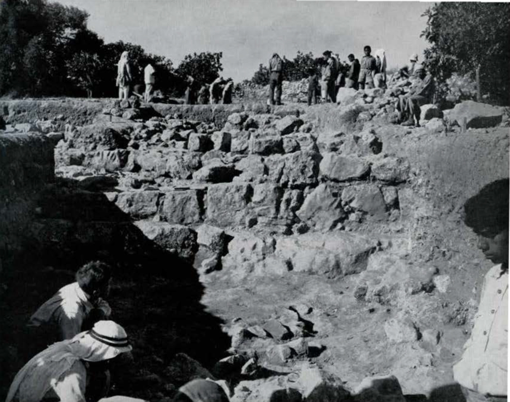 Men excavating a city wall made of large stones.