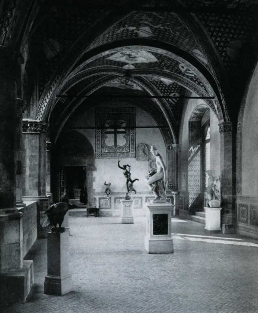 View of a palatial hall with vaulted ceilings displaying statues on pedestals.