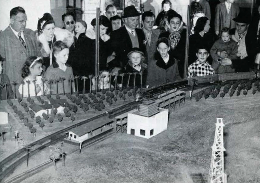 A crowd gathered around a miniature town and  traintrack diorama.